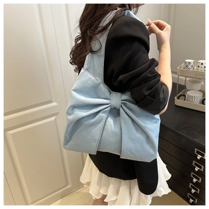 Detail of light blue denim tote bag with oversized bow design worn by a model