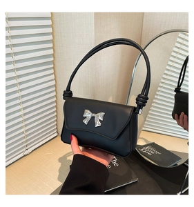Detail of a black leather shoulder bag with a silver metal bow and knotted strap design