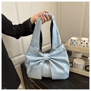 Detail of light blue denim handbag featuring a large bow shape and knotted top handle