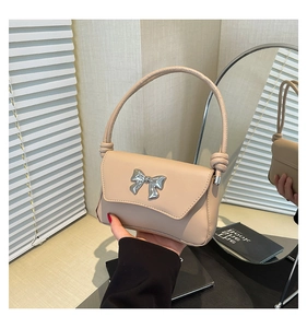 Detail of beige leather handbag featuring a large silver bow buckle and twisted handle