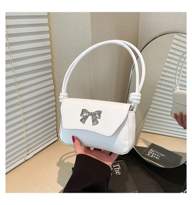 Detail of white leather shoulder bag featuring a silver metal bow buckle and knotted strap