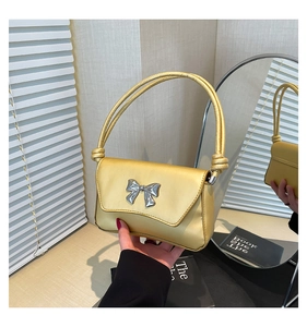 Detailed macro view of a metallic light gold square bag with a silver bow and thin straps