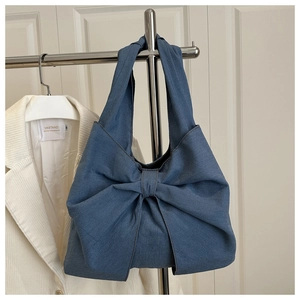 Chic denim tote bag with oversized bow detail on minimalist white corduroy display