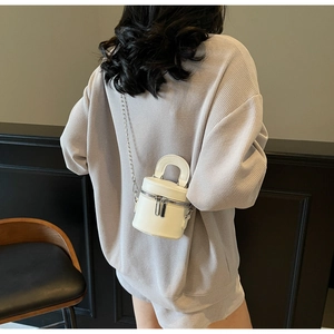Rückansicht einer weißen Zylindertasche mit silberner Kette, von einem Modell getragen