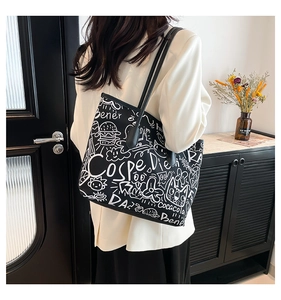 Detail of a black leather tote bag featuring white street style graffiti patterns and straps
