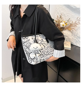 Close-up of graffiti tote bag with black cartoon doodles and a white plush cloud charm