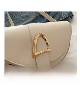 Close-up of the stylish golden triangular metal buckle on a cream white saddle bag