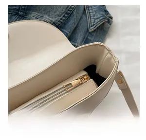 Detailed close-up of smooth gold zipper and stitching on a beige leather saddle bag