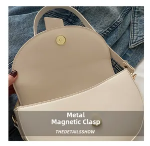 Close-up of the metal magnetic clasp and neat stitching on a cream saddle bag