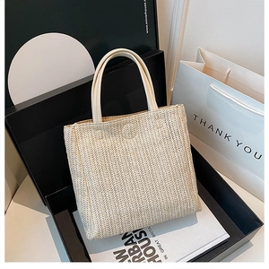 Close-up of woven straw tote bag with leather handles in luxury gift box display