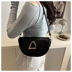 Détail d'un sac besace en cuir noir doté d'une grande boucle métallique dorée triangulaire