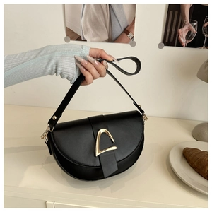 Détail d'un sac besace noir mat avec boucle en D dorée dans un décor de café parisien chic
