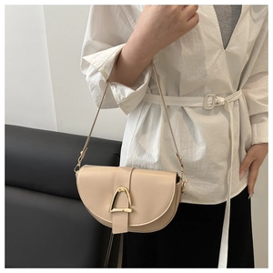 Detail of beige crescent saddle bag with signature gold D-buckle on a white outfit