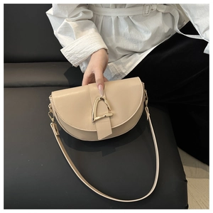 Mannequin tenant un sac besace beige avec boucle triangulaire dorée sur fond sombre
