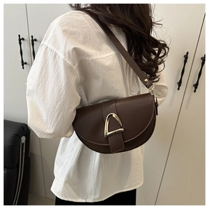 Detail of dark brown vintage saddle bag with gold horseshoe buckle worn by a model