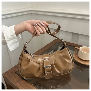 Close-up of caramel brown glossy patent leather shoulder bag with buckle strap details