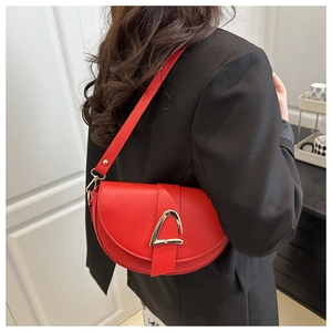 Détail du sac selle rouge avec boucle triangle dorée porté sur un blazer noir