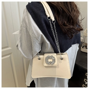 Model wearing a cream-colored shoulder bag with a crystal buckle and chain strap