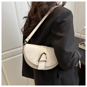 Détail d'un sac besace ivoire avec boucle dorée triangulaire porté sur un blazer noir