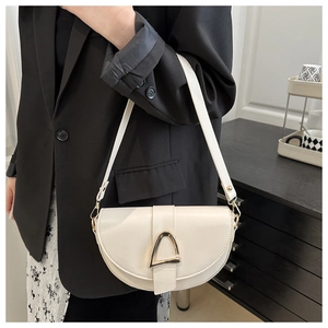 Détail d'un sac besace blanc avec boucle triangle dorée porté à l'épaule par un mannequin