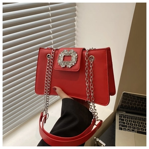 Close-up of bright red shoulder bag featuring sparkling rhinestone buckle and silver chain