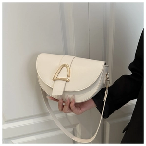 Détail d'un sac selle beige avec une boucle dorée en forme de D et une bandoulière en cuir