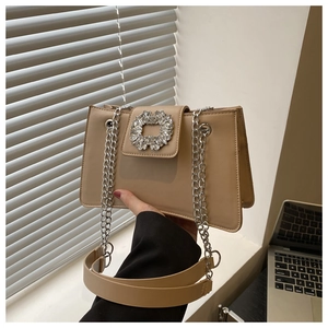 Close-up of khaki shoulder bag featuring a large sparkling crystal buckle and chain strap