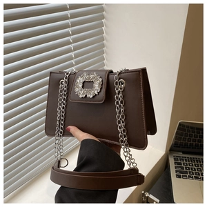 Detail view of the dark brown leather handbag with sparkling rhinestone buckle and silver chain