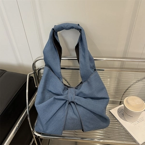 Blue denim tote bag featuring a large bow design and integrated top handles on a shelf