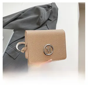 Detail of beige textured shoulder bag with silver 'M' metal buckle on a grey blazer