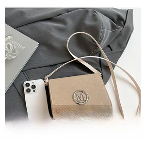 Detail view of small square bag with silver M logo and phone for size reference