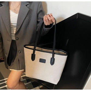 Close-up of a large canvas tote bag with black leather straps on a model in a grey suit