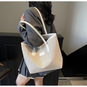 Detail view of a large canvas tote bag with white leather trim worn by a model