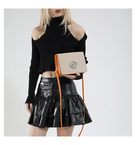 Detail view of stylish crossbody bag featuring orange contrast and silver M logo