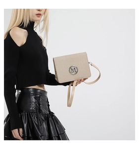 Detail of beige woven square bag with silver metal M logo worn by model on black outfit