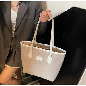 Detail of canvas tote bag with contrast leather trim and handles on model's shoulder
