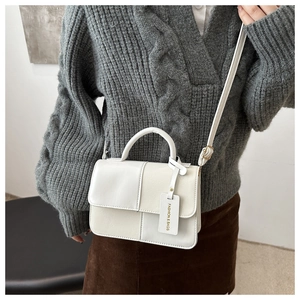 Detail of white patchwork square bag with gold tag and textured leather on grey sweater