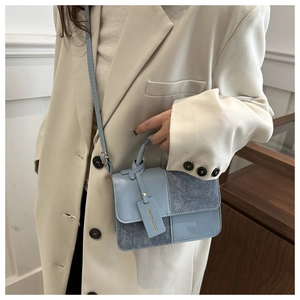 Detail of light blue crossbody bag with mixed textures and fashion hangtag shown on model