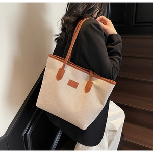 Detail of canvas tote bag with brown leather trim shown during indoor model wear