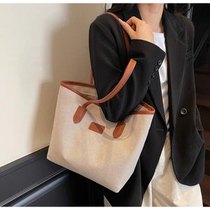 Detail of canvas tote bag with brown leather handles worn over a black blazer