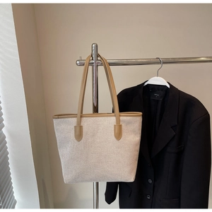 Detailed close-up of beige canvas tote bag with brown leather trim and handles