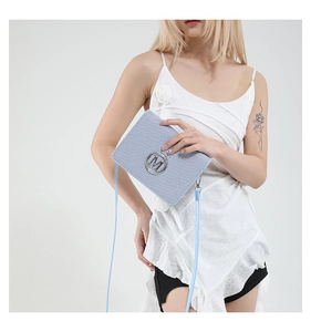 Detail of light blue camera bag with silver M logo and slim leather shoulder strap