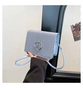Detailed texture of light blue shoulder bag with silver metallic M logo and grainy fabric