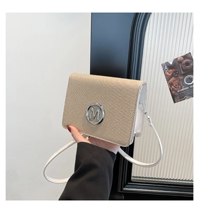 Detailed shot of beige woven bag featuring a silver metal M logo and white leather strap