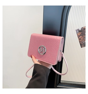 Detail of pink textured crossbody bag with silver M logo and adjustable leather strap
