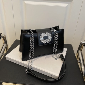 Elegant black rhinestone-encrusted shoulder bag with silver chain strap on white book