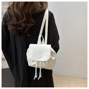 Detail of white mini backpack with drawstring flap and fashion patch on black outfit