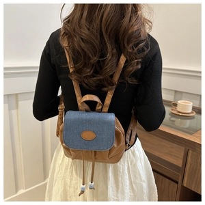 Detail view of mini backpack featuring blue denim flap and brown leather with Fashion label