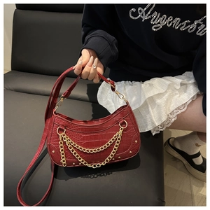Close-up of dark red crocodile pattern handbag with gold metal chains and rivets