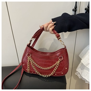 Detail of red crocodile embossed baguette bag with golden chains and rivets